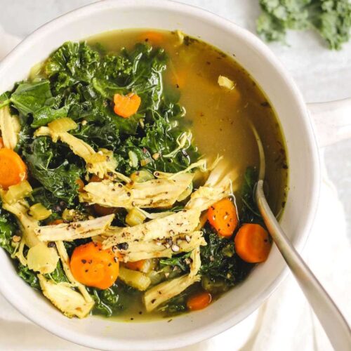 Chicken and kale soup in a white soup bowl with a spoon.