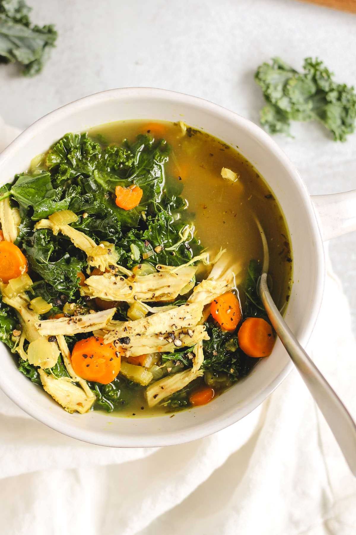 Chicken and kale soup in a white soup bowl with a spoon.