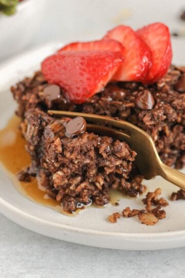 Gold fork cutting a bite off of a piece of chocolate baked oats topped with strawberries.