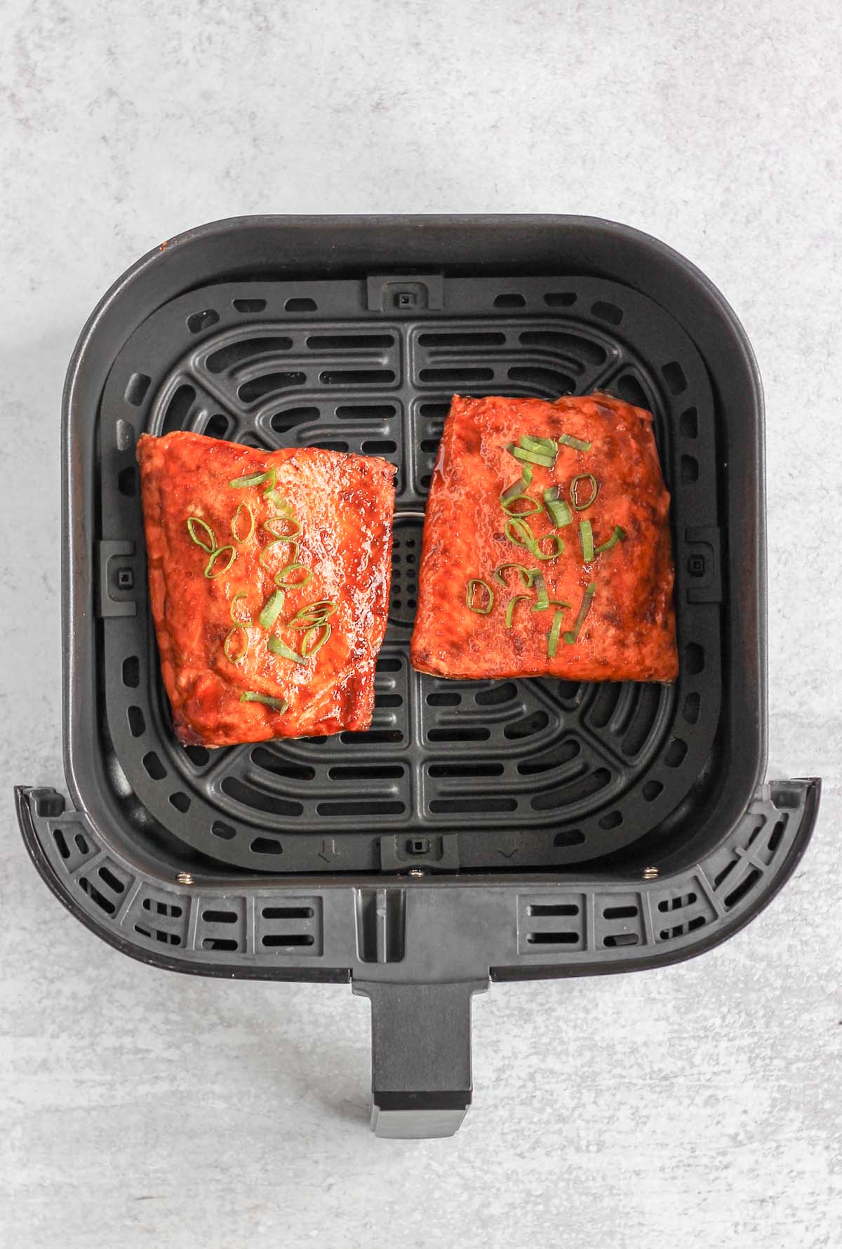 Cooked salmon fillets in an air fryer basket.