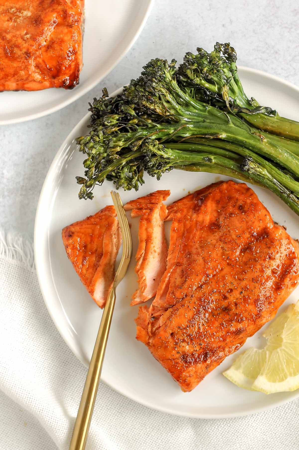 A gold fork cutting into a salmon fillet on a plate with broccolini.