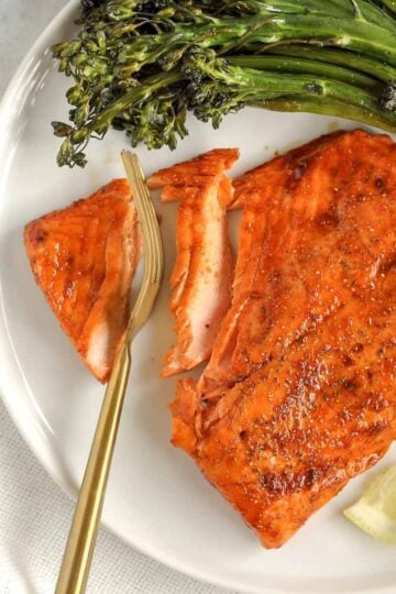 A gold fork cutting into a salmon fillet.