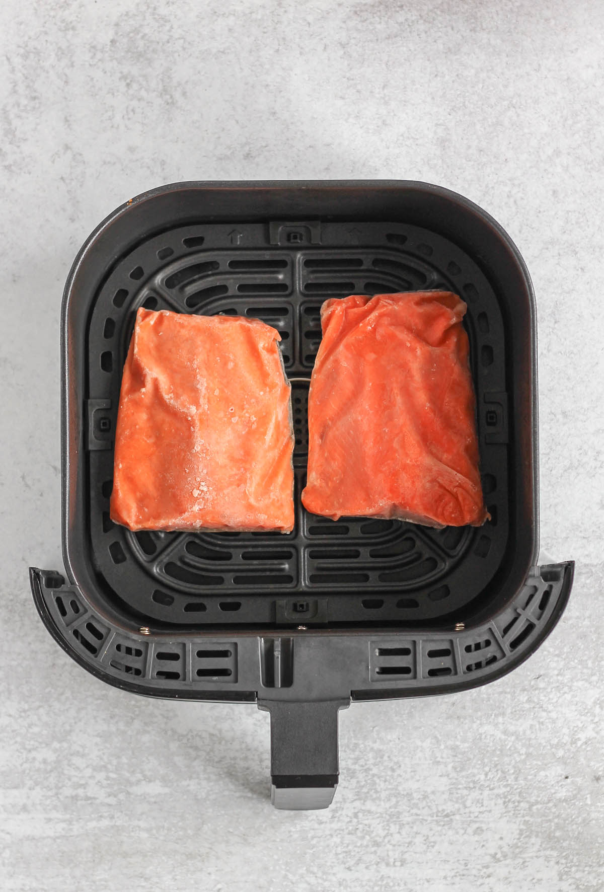 Frozen salmon fillets in an air fryer basket.