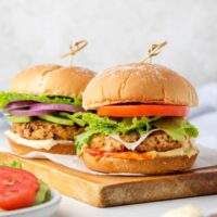 Two air fried turkey burgers with buns on a wood cutting board.