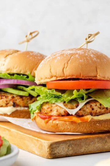 Two air fried turkey burgers with buns on a wood cutting board.