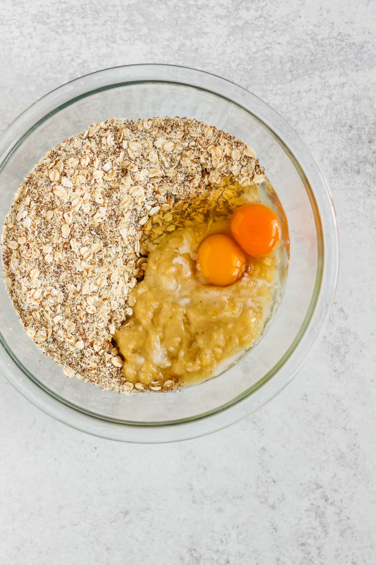 Mixing bowl with oats and almond flour on one side and eggs and mashed banana on the other side.