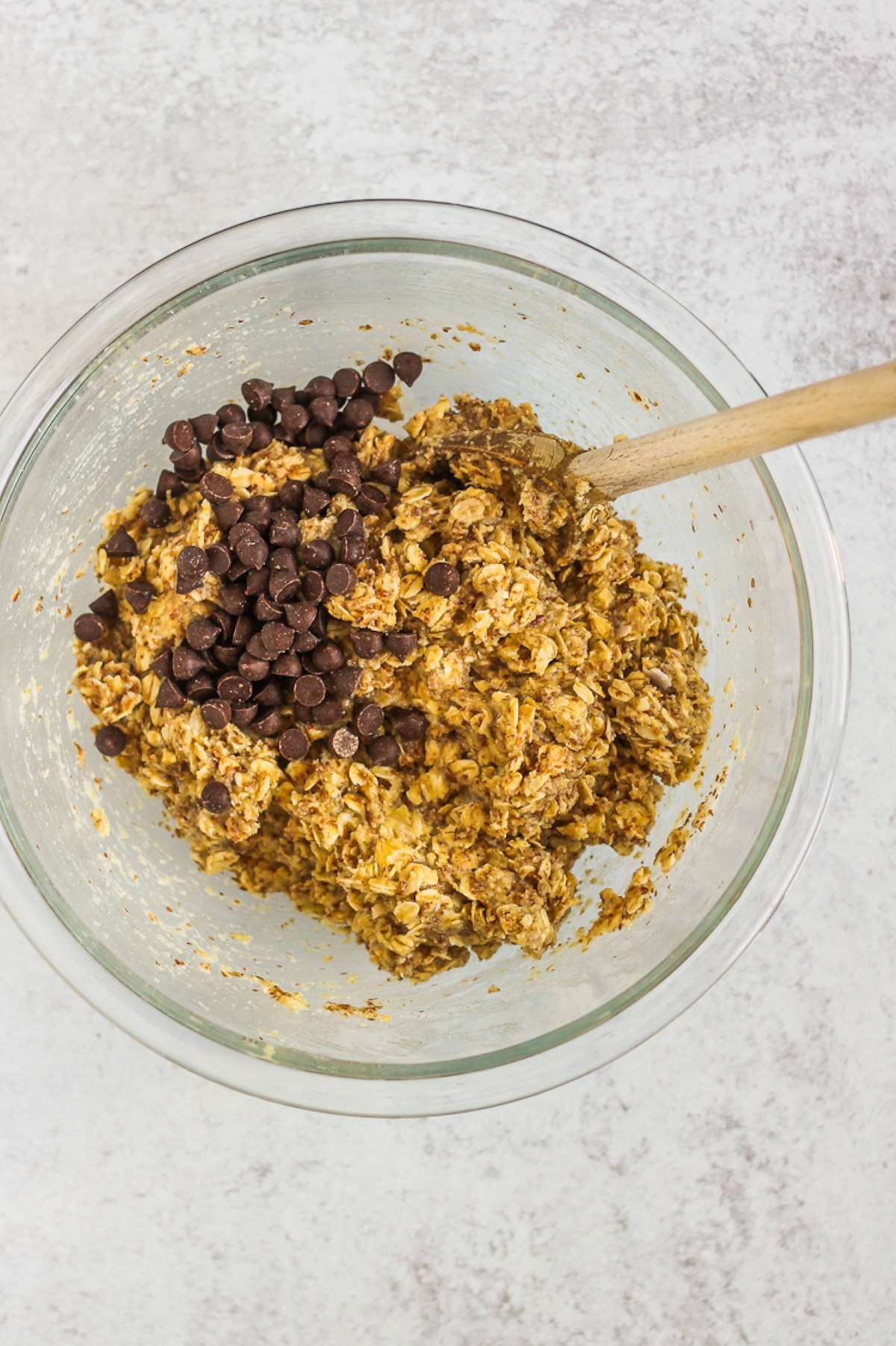 Oat mixture in a mixing bowl with chocolate chips and a wooden mixing spoon.