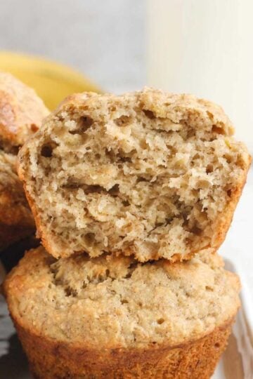 Banana muffins stacked 2 high with top one cut open to show texture.