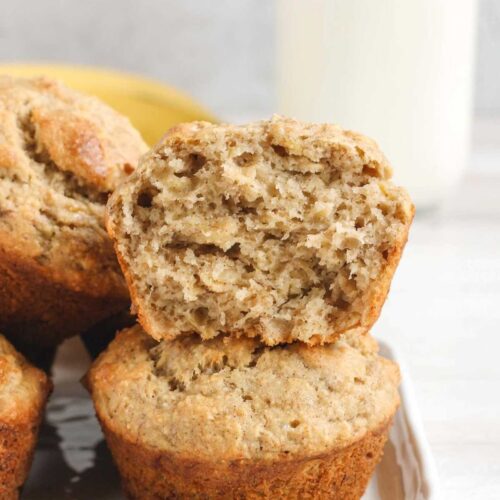 Banana muffins stacked 2 high with top one cut open to show texture.