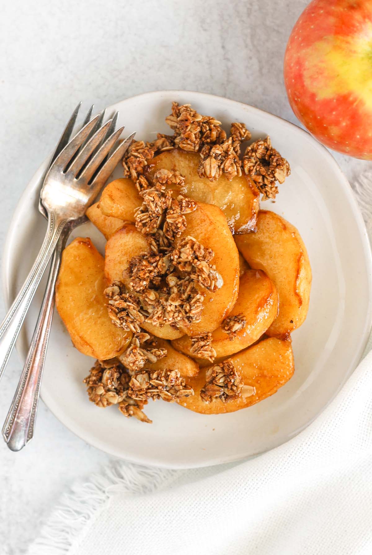 Air fried apples topped with granola on a white plate with two vintage forks on the plate with an apple off to the side.