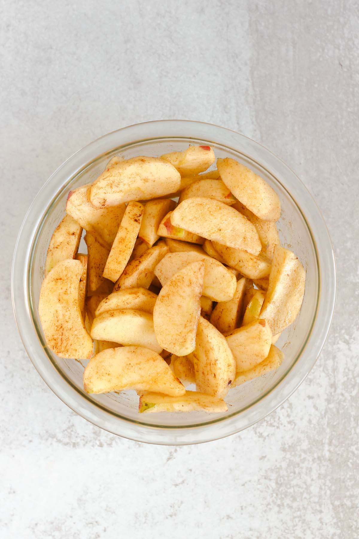 Apple slices mixed with cinnamon in a glass mixing bowl.