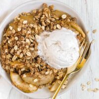 Individual serving of apple crisp on a white plate with a gold fork with a scoop of ice cream on top.