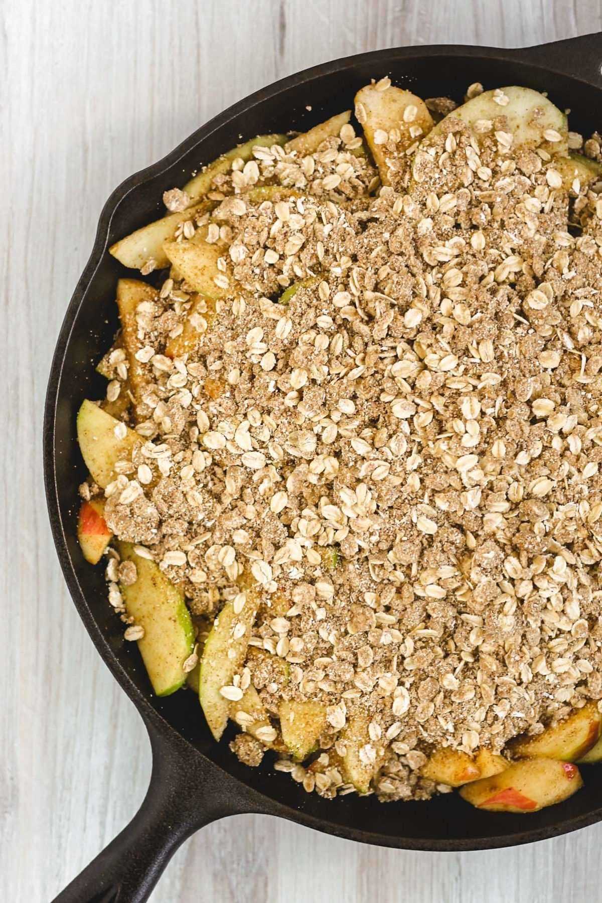 Sliced apples topped with oat crumble topping in a cast iron skillet before baking.
