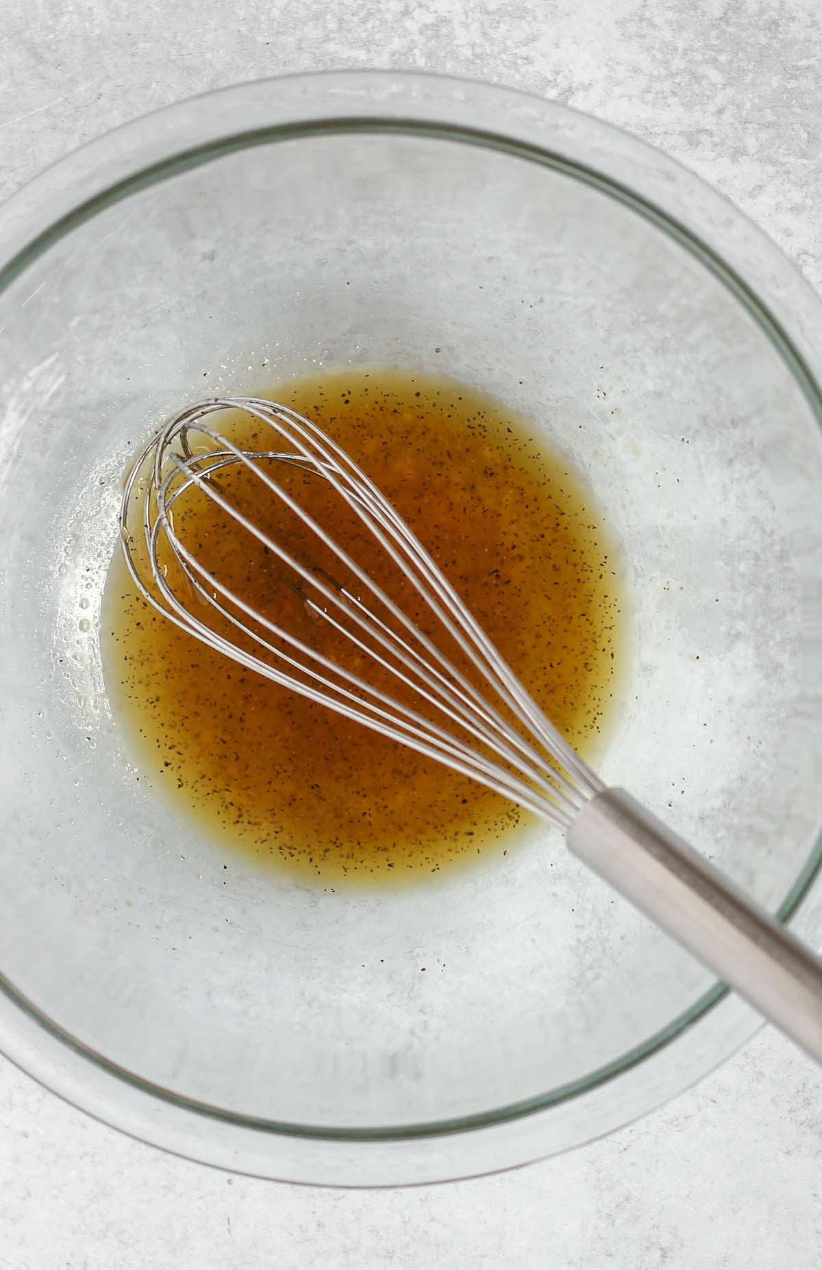 Wire whisk mixing honey marinade in a small glass mixing bowl.