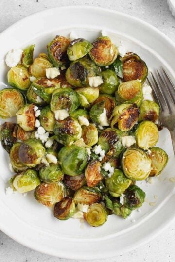 Roasted Brussels sprouts with goat cheese on a round plate with a vintage fork.