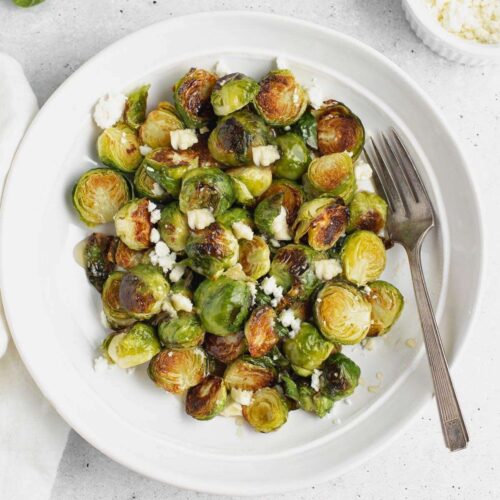 Roasted Brussels sprouts with goat cheese on a round plate with a vintage fork.