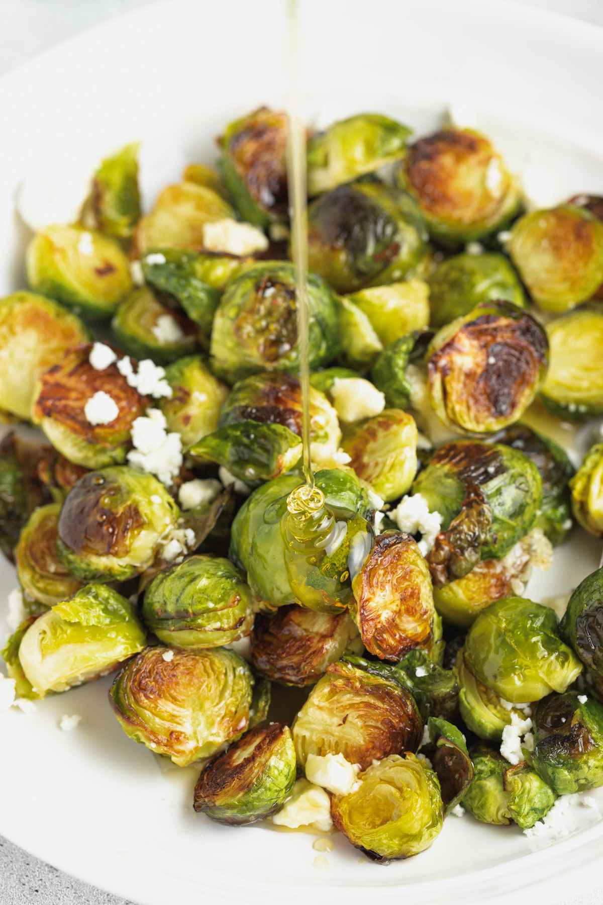 Honey being drizzled over cooked Brussels sprouts.