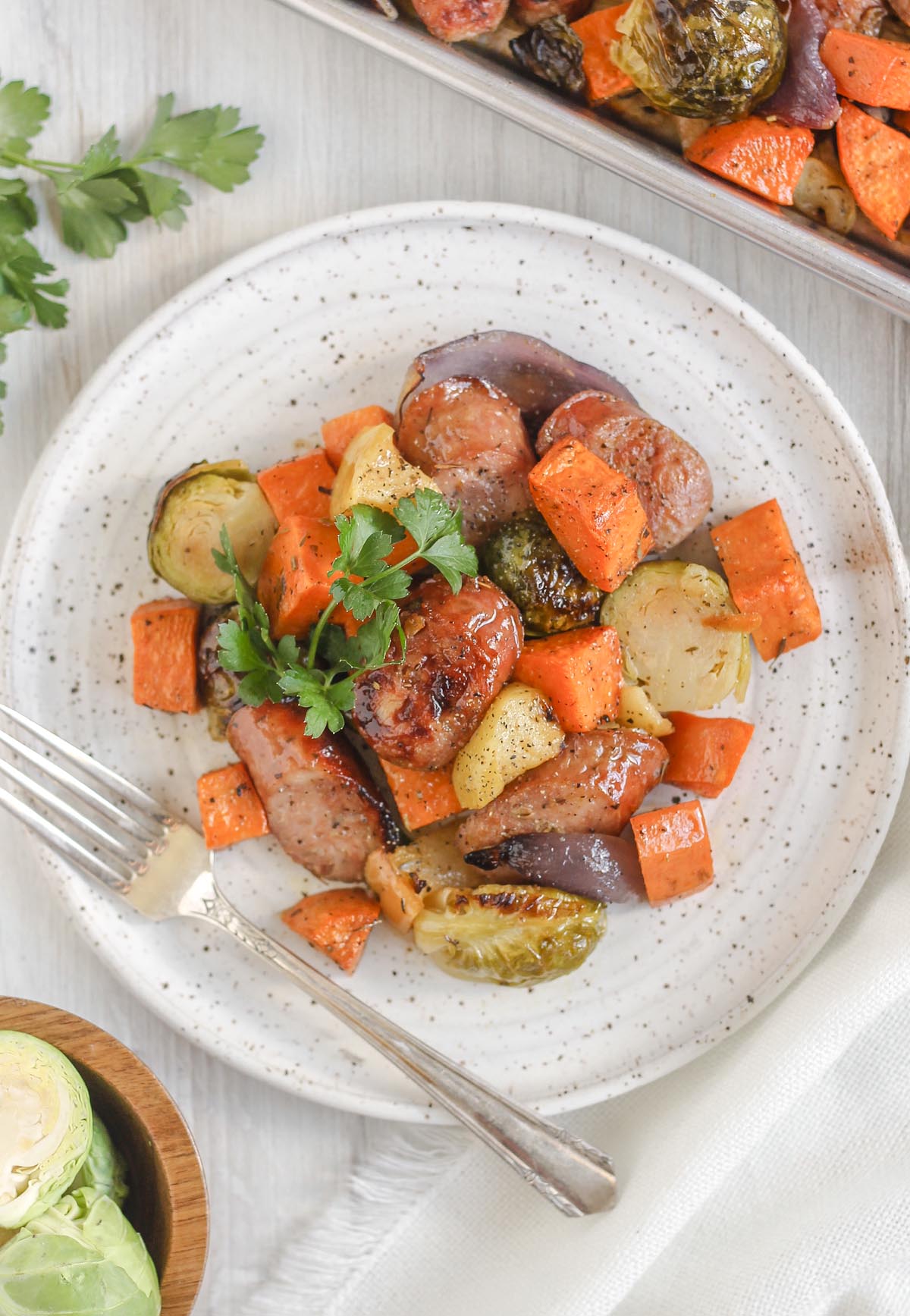 Chicken sausage with roasted veggies on a round white plate topped with parsley with a vintage fork on the plate.