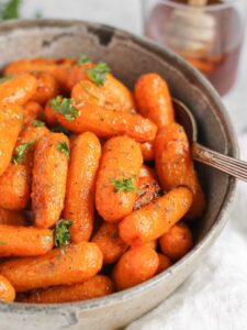 Air fryer roasted baby carrots in a gray serving bowl with a cup of honey in the back ground.