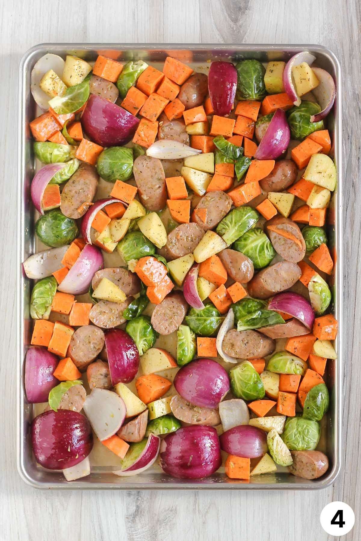 Sliced chicken sausage, chopped vegetables, and chopped apple on a large baking sheet before being cooked.