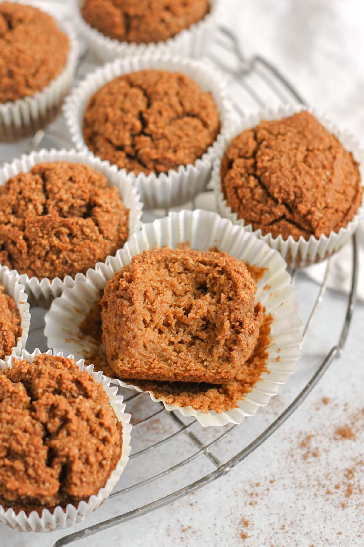 Paleo pumpkin muffins on a round wire cooling rack with a bite taken out of the center muffin laying in a white paper muffin liner.