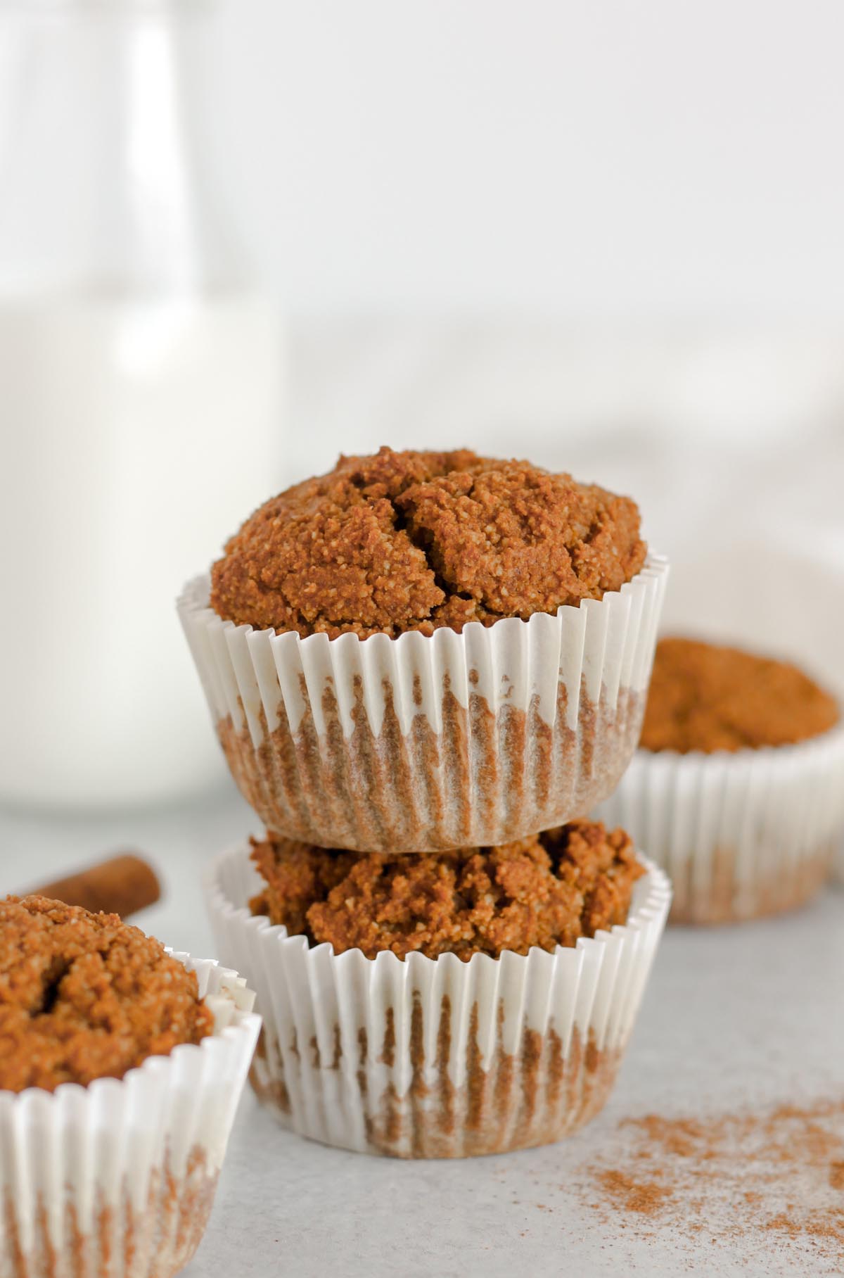 Paleo pumpkin muffins stacked two high with a jar of milk and additional muffins in the background.