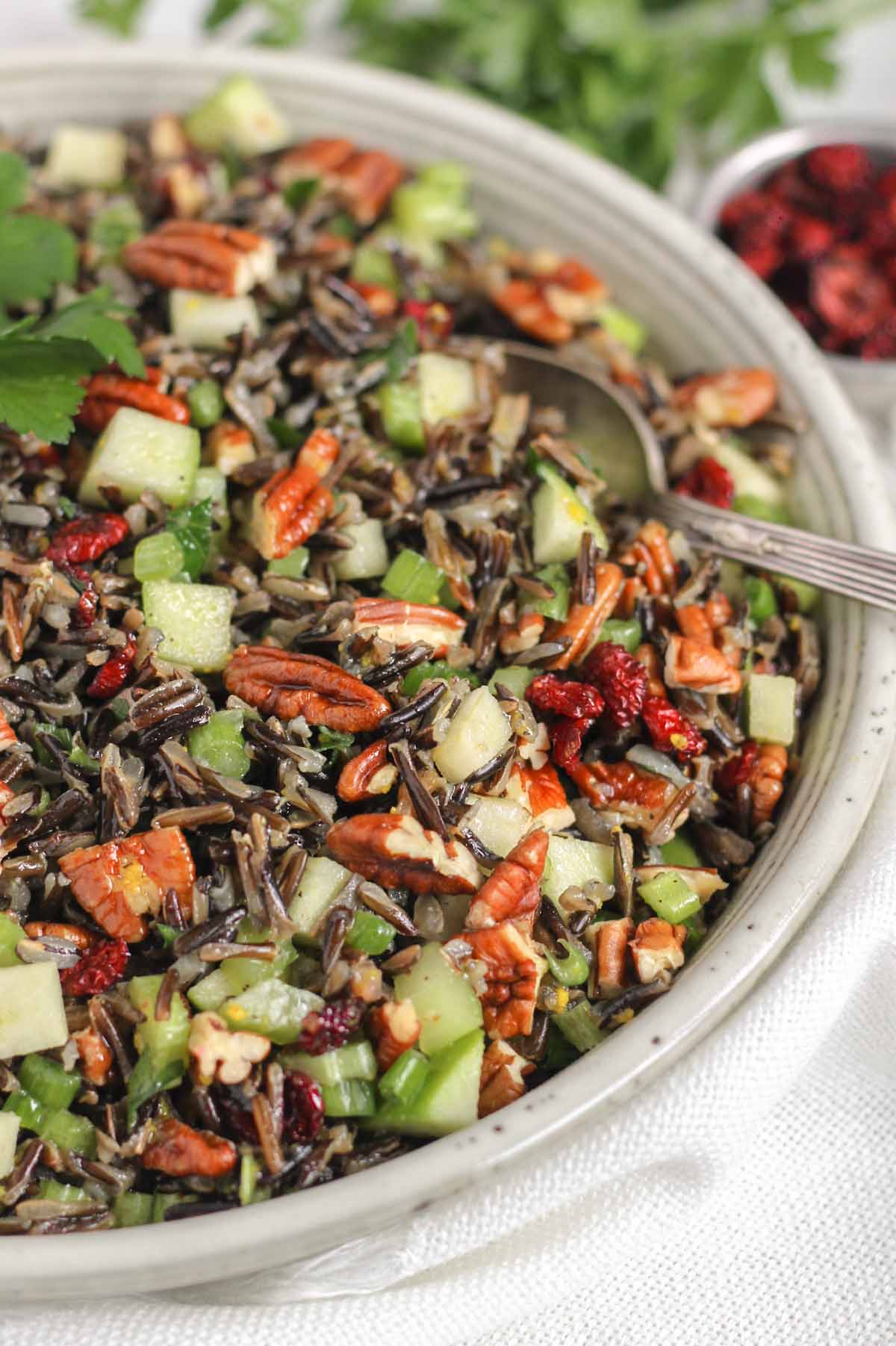 Cold wild rice salad with a vintage serving spoon in a ceramic serving bowl.