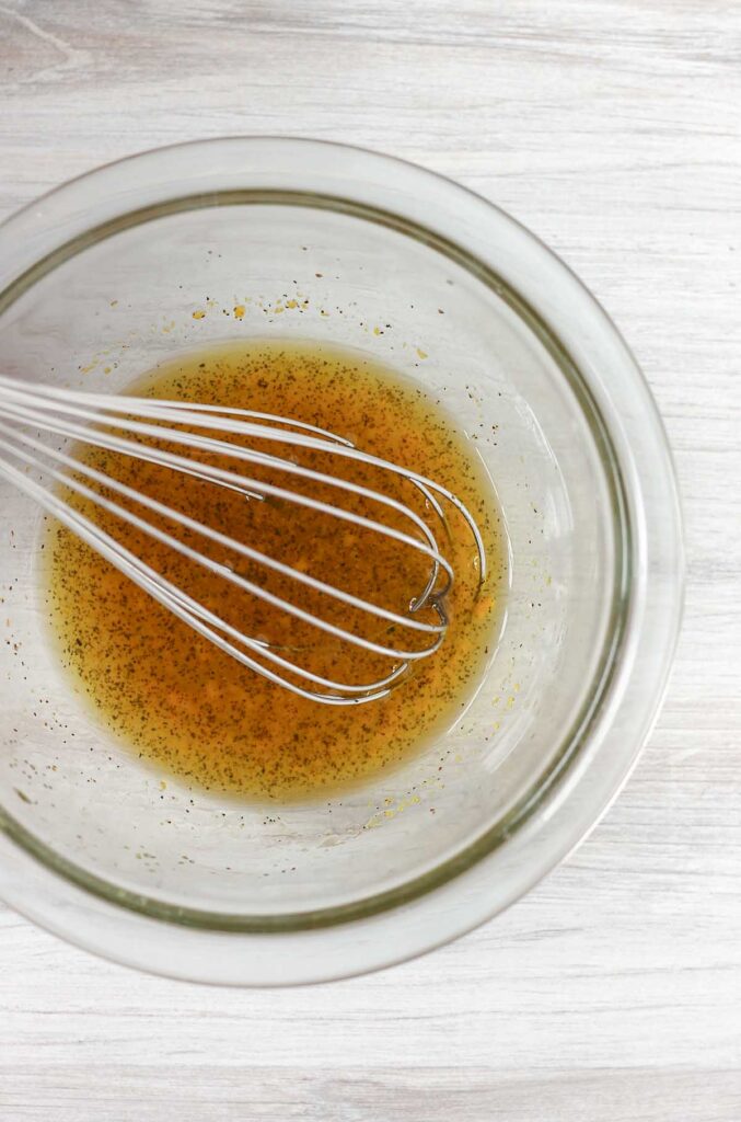 Orange vinaigrette dressing in a mixing bowl with a whisk.