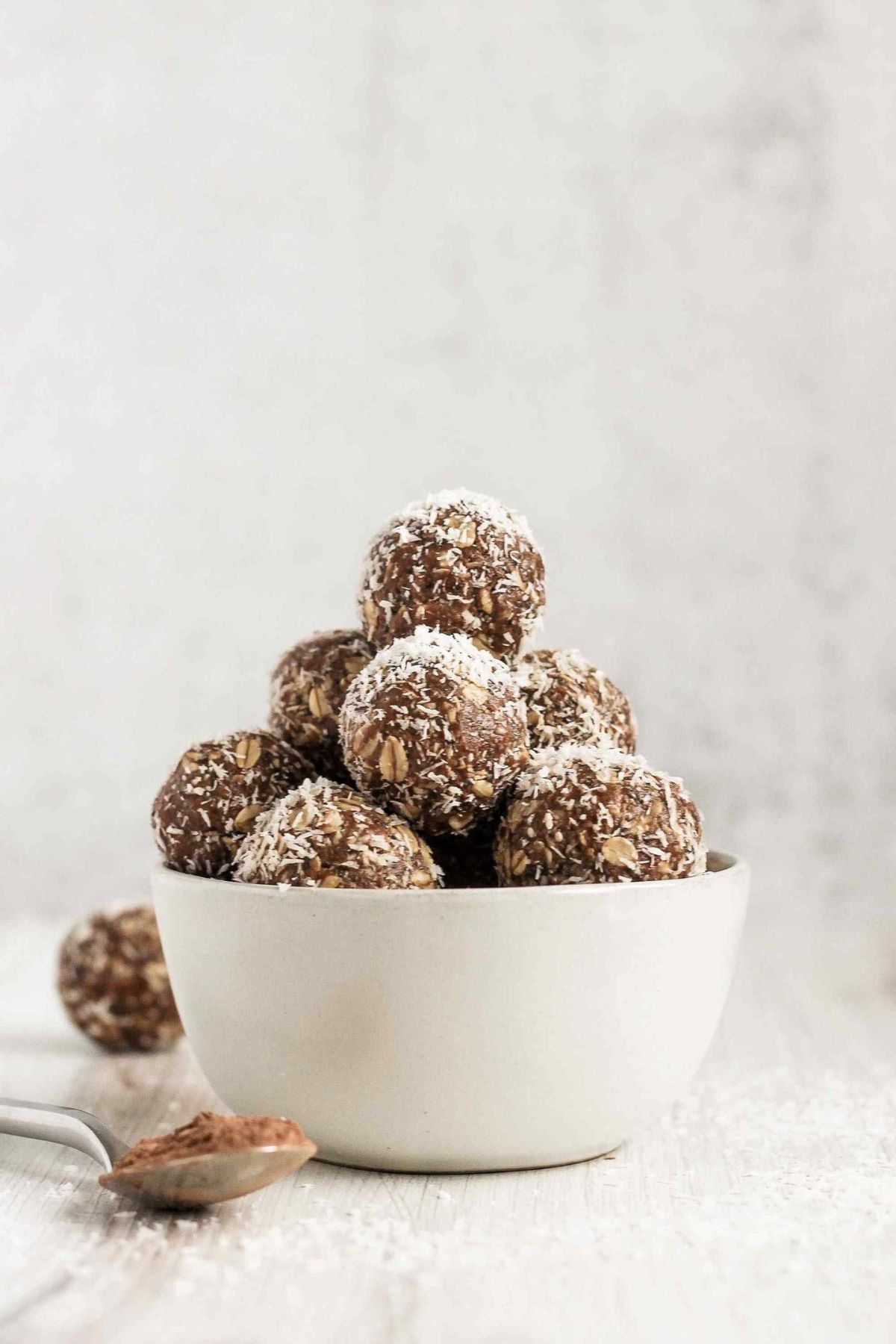 Chocolate peanut butter balls sprinkled with coconut flakes stacked in a small white bowl.