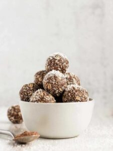 Chocolate peanut butter balls sprinkled with coconut flakes stacked in a small white bowl.
