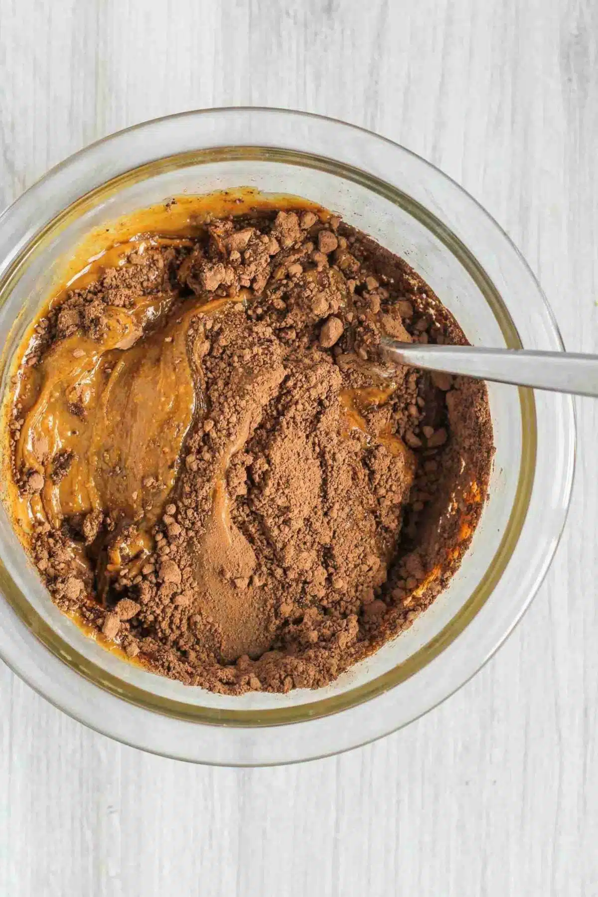 Peanut butter, honey, and cacao being mixed together in a glass mixing bowl.