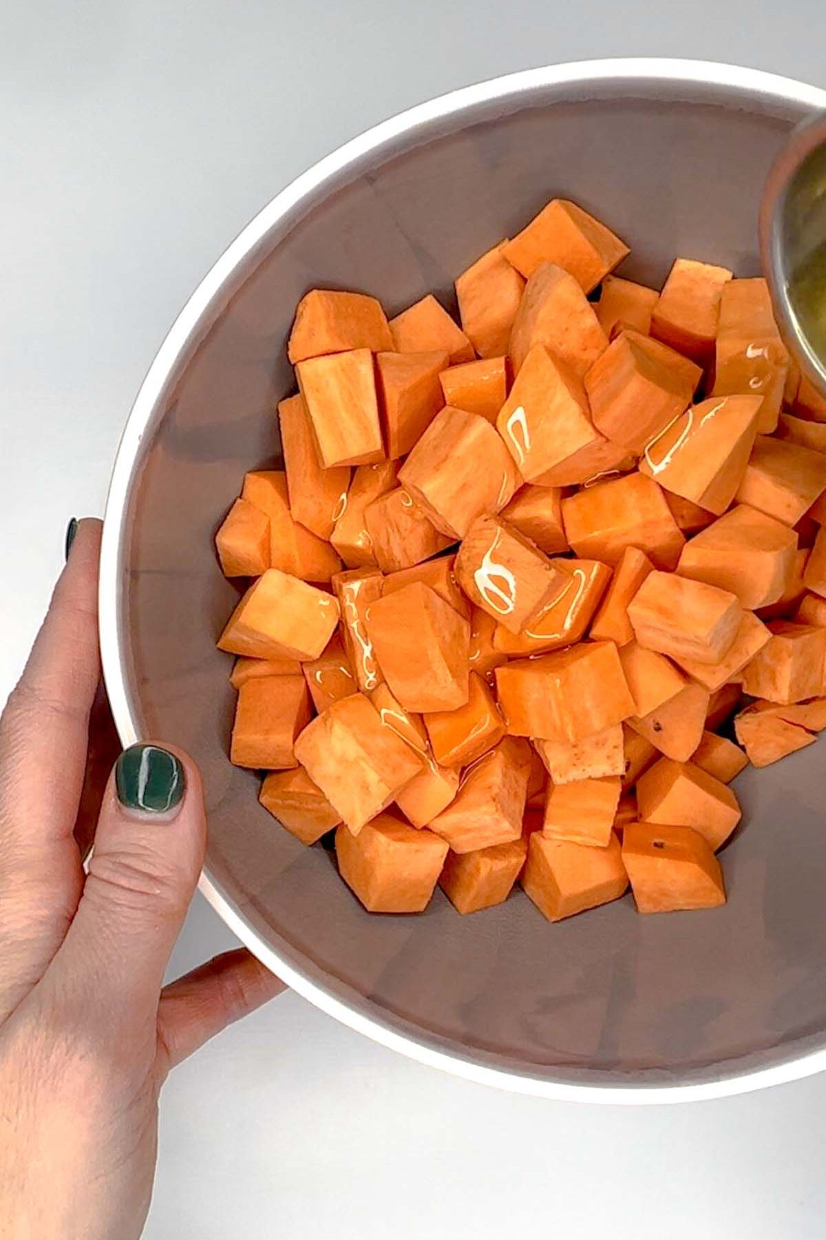 Sweet potato cubes in a gray mixing bowl with oil drizzled on top.