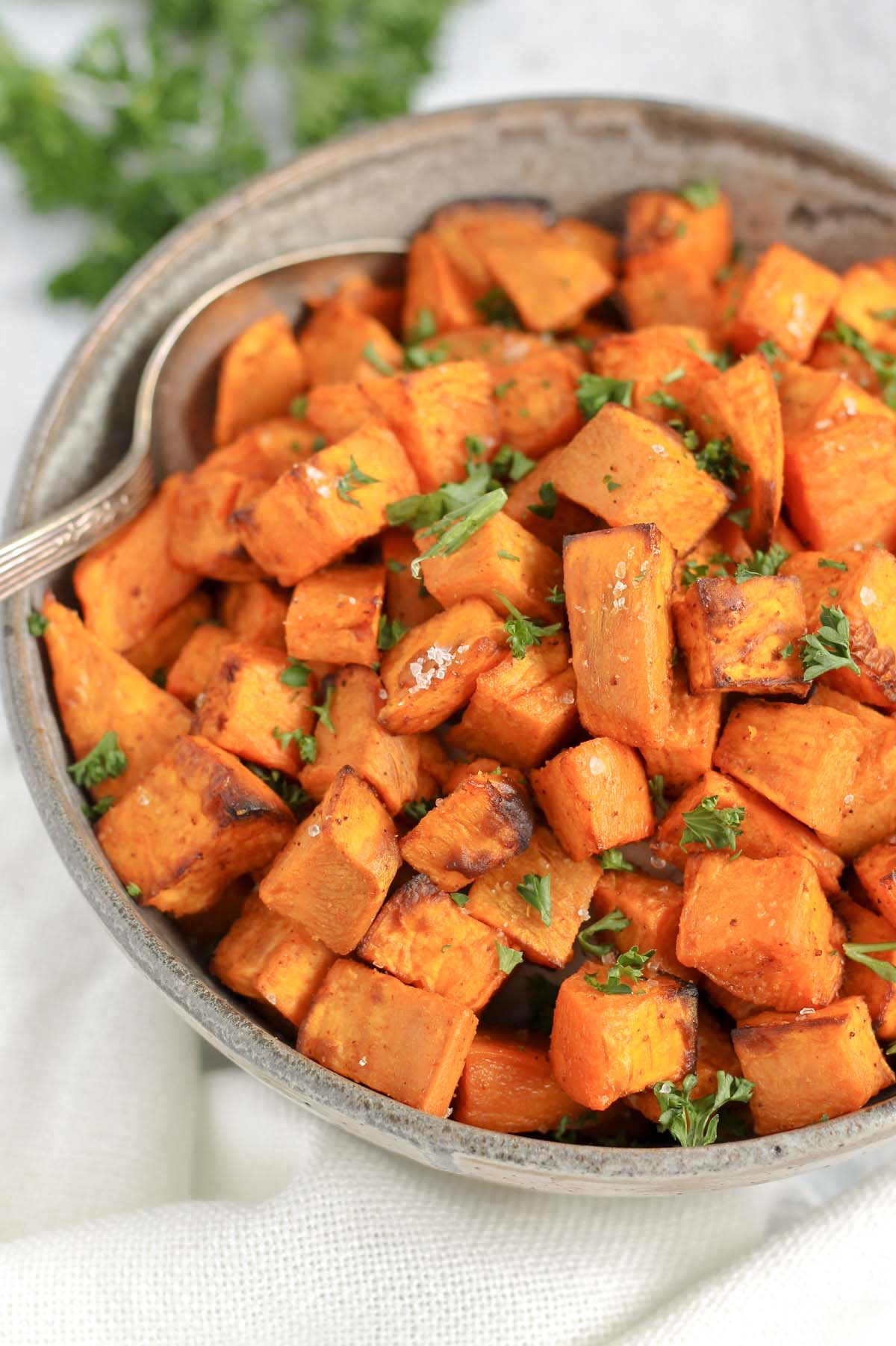 Air fried sweet potato cubes sprinkled with fresh parsley in a gray serving bowl with a serving spoon.