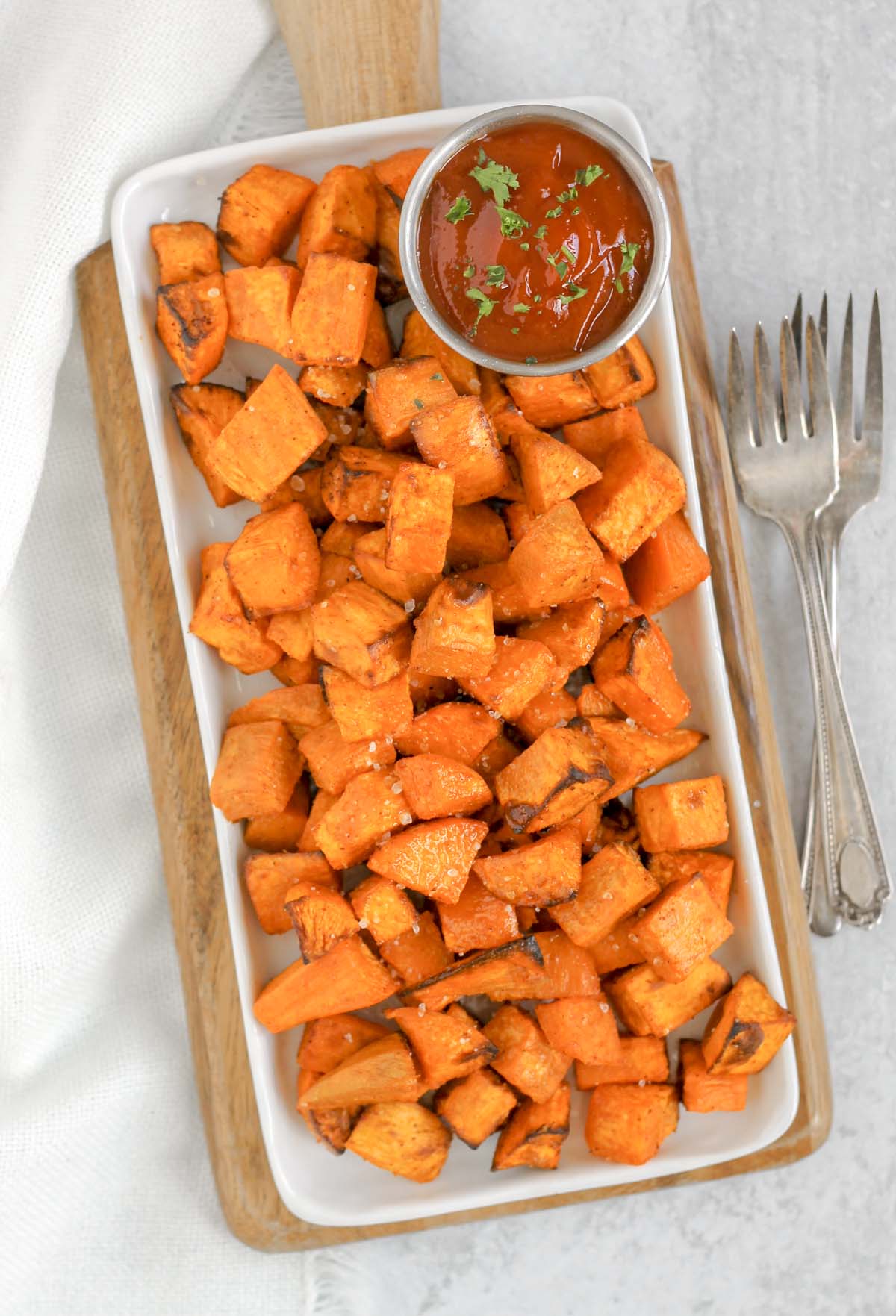 Roasted sweet potato cubes on a white rectangular plate with a side of ketchup.