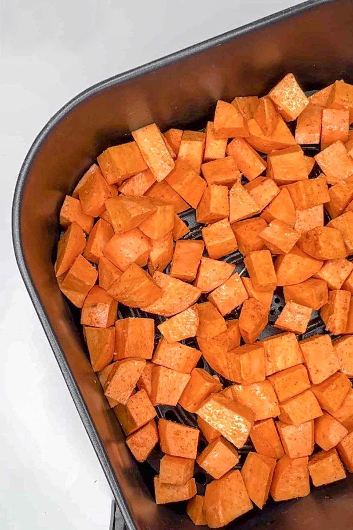 Uncooked sweet potato cubes in an air fryer basket.