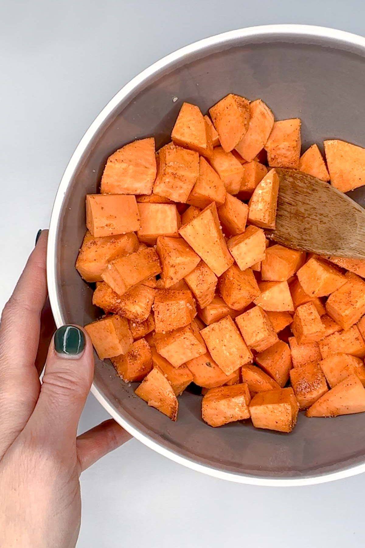 Sweet potato cubes mixed with seasoning in a gray mixing bowl.