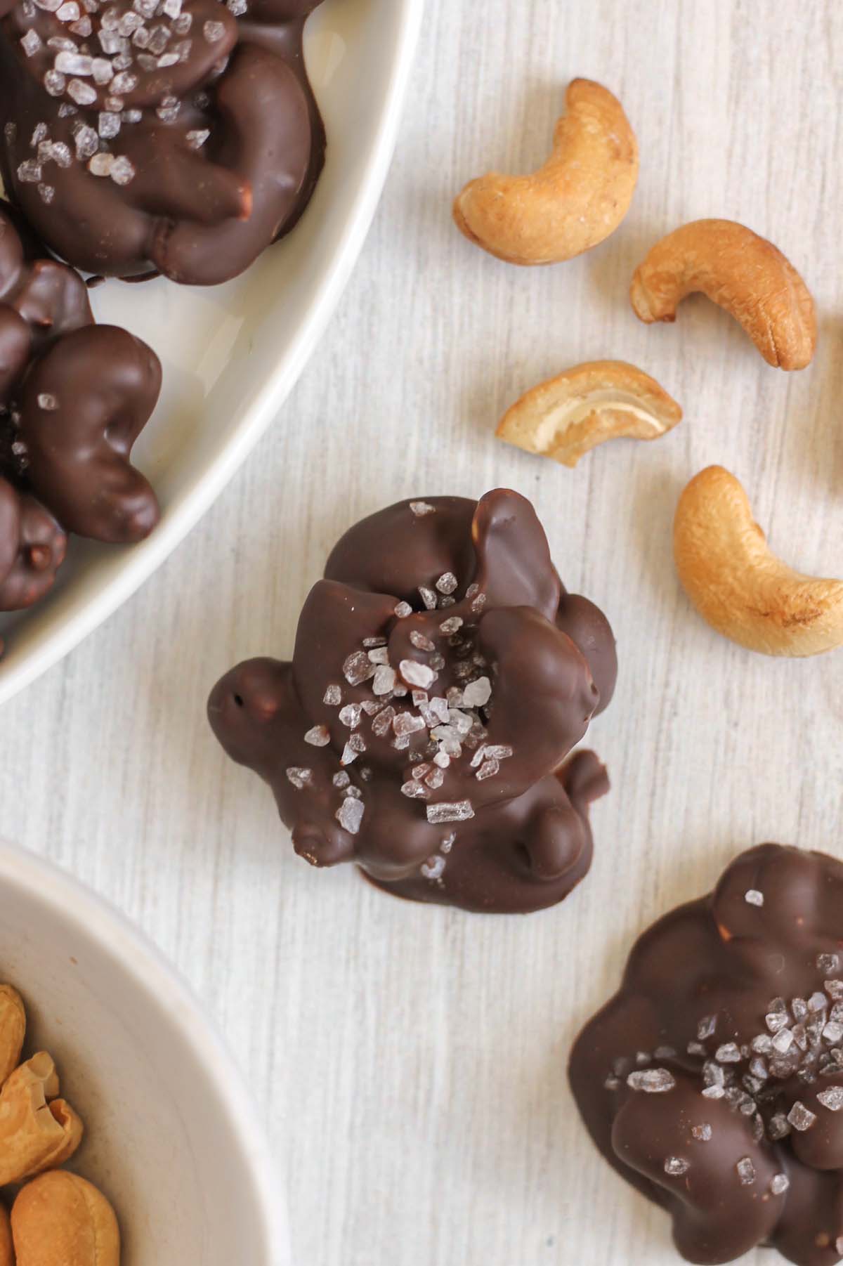 Close-up of chocolate cashew cluster with raw cashews sprinkled on the side.