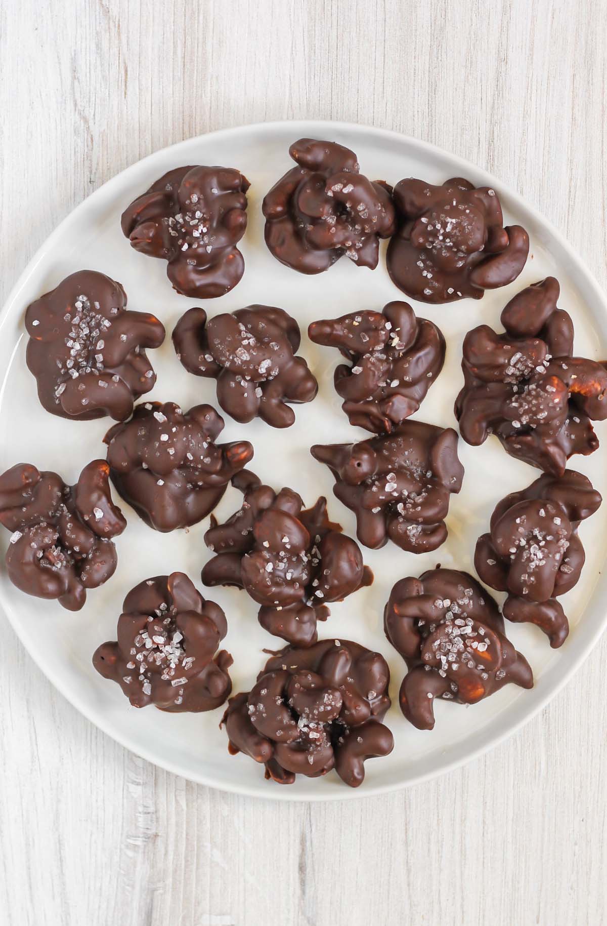 Chocolate covered cashew clusters topped with sea salt on a round white plate.