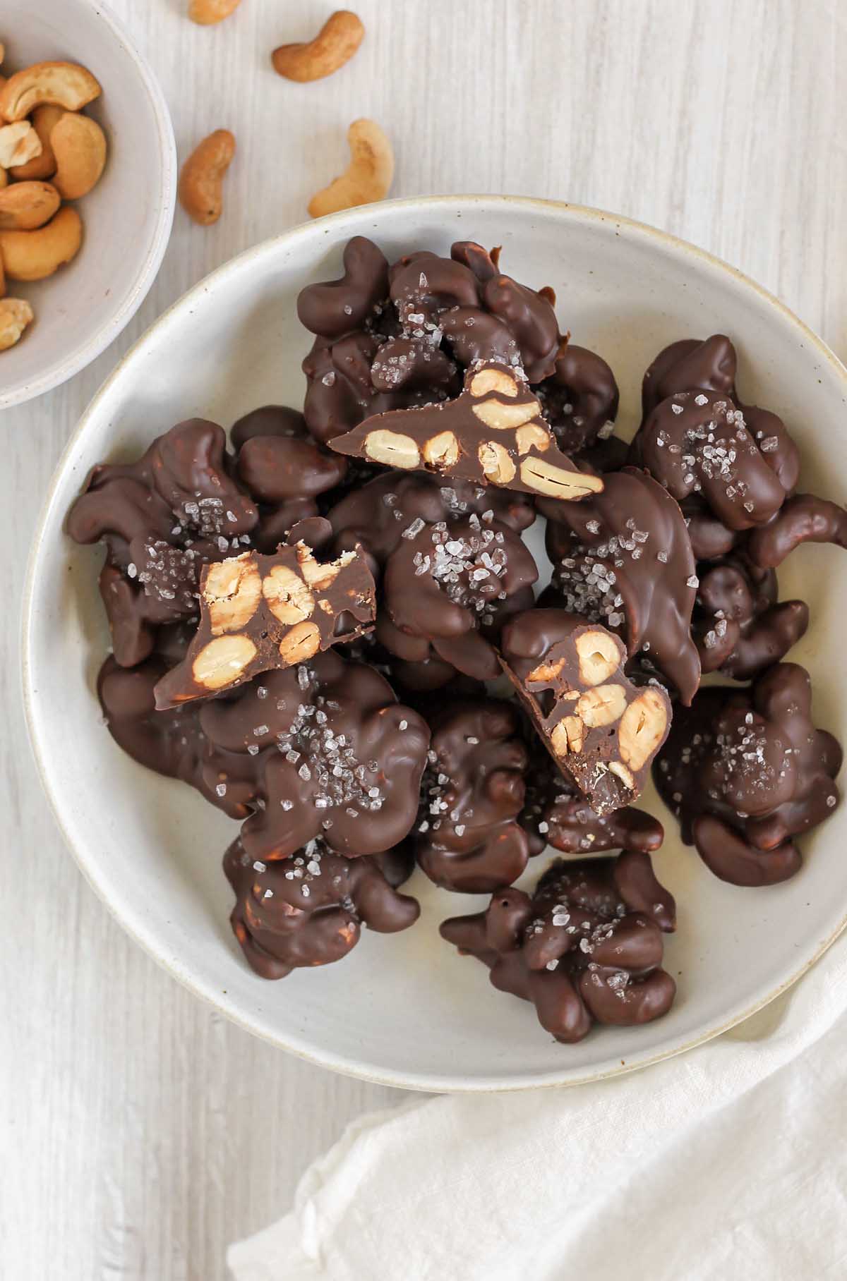 Overhead view of chocolate cashew clusters on a plate. Some cashew clusters cut in half to show center.