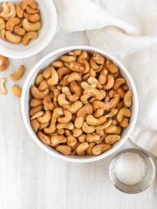 Roasted cashews in a bowl with small bowls of cashews and sea salt off to the side.