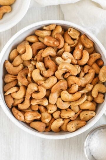 Roasted cashews in a bowl with small bowls of cashews and sea salt off to the side.