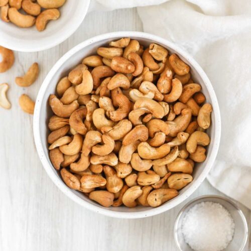 Roasted cashews in a bowl with small bowls of cashews and sea salt off to the side.