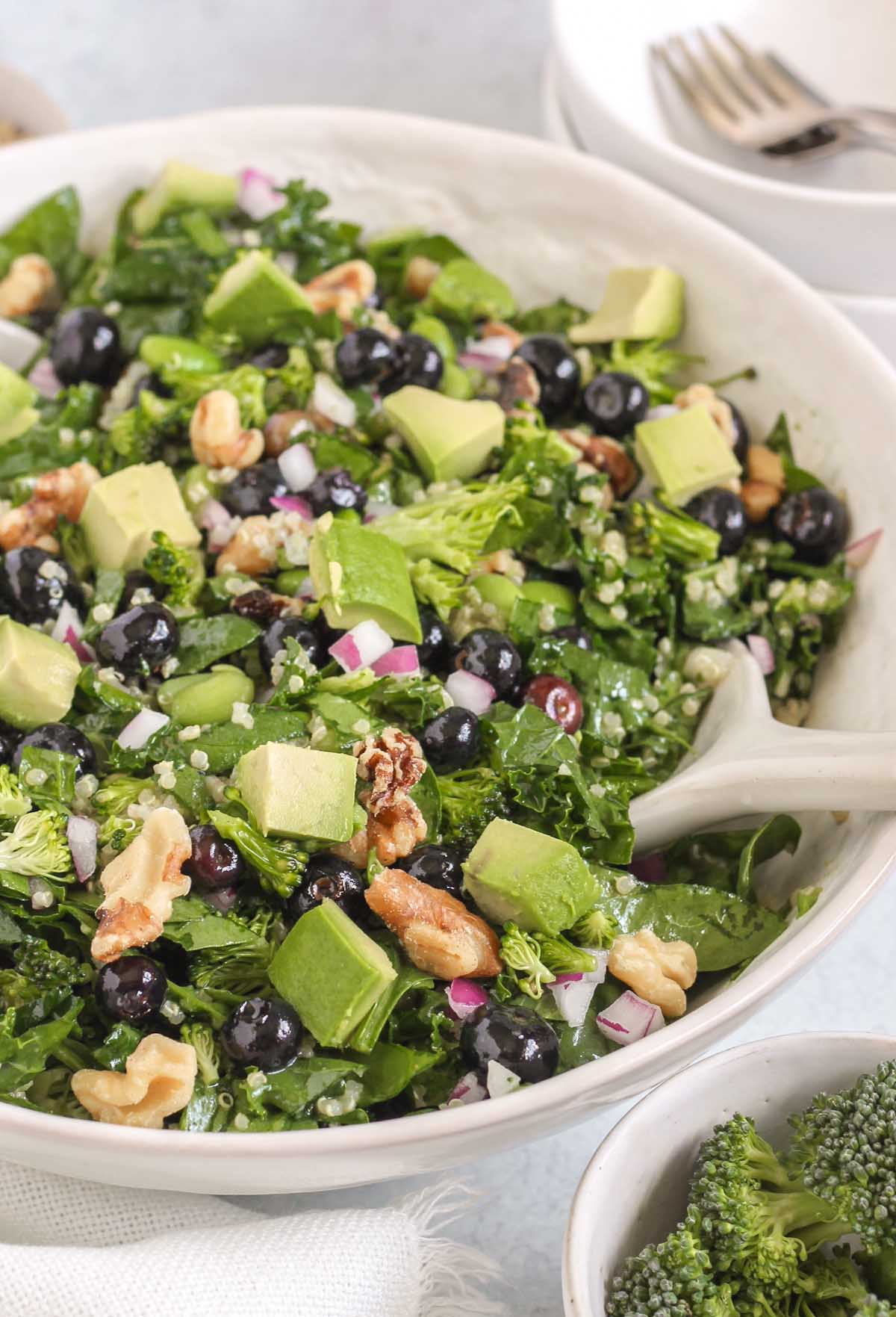 Superfood salad in a large white bowl with two small salad bowls and forks in the background.