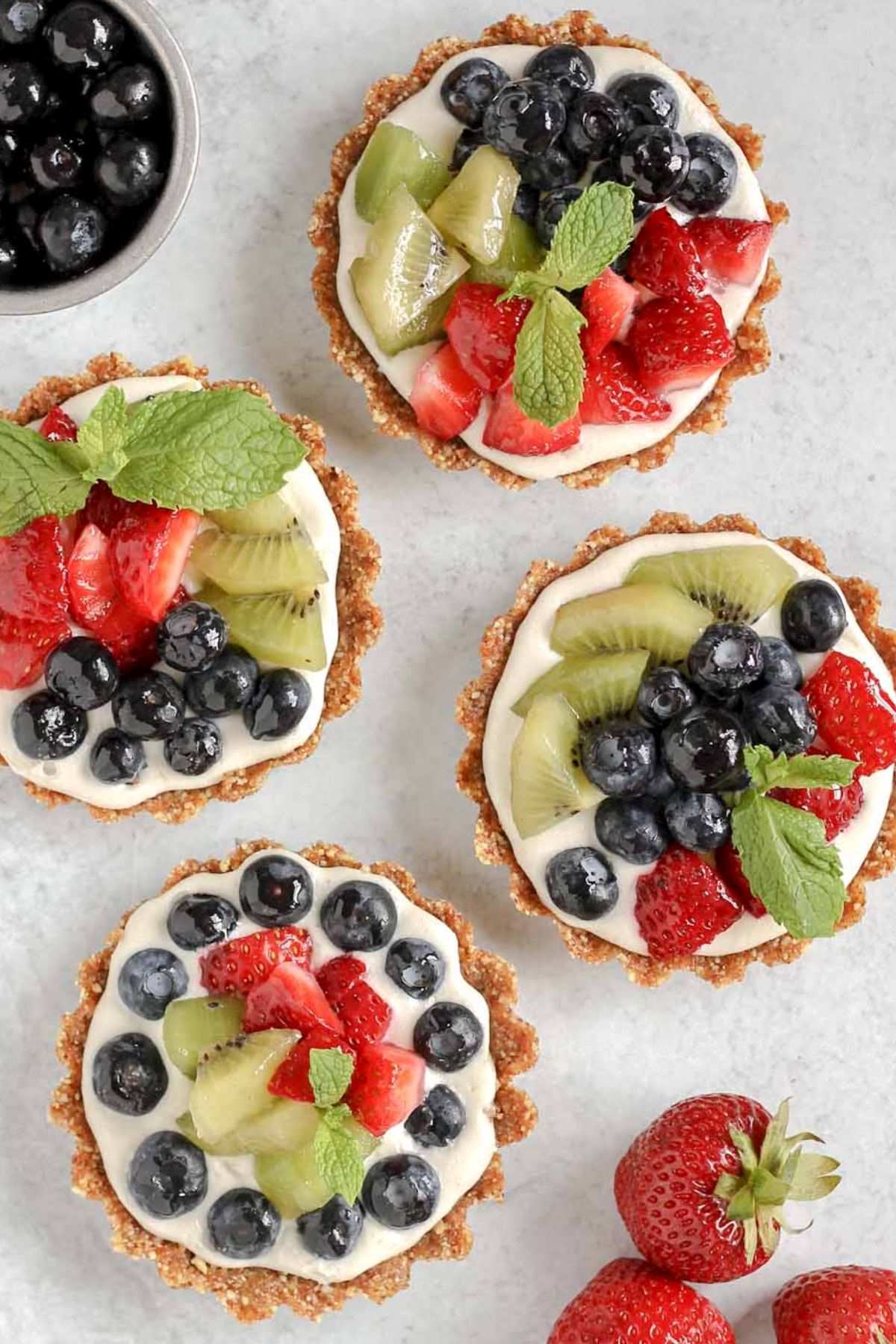 Four mini fruit tarts laid out on a gray surface.