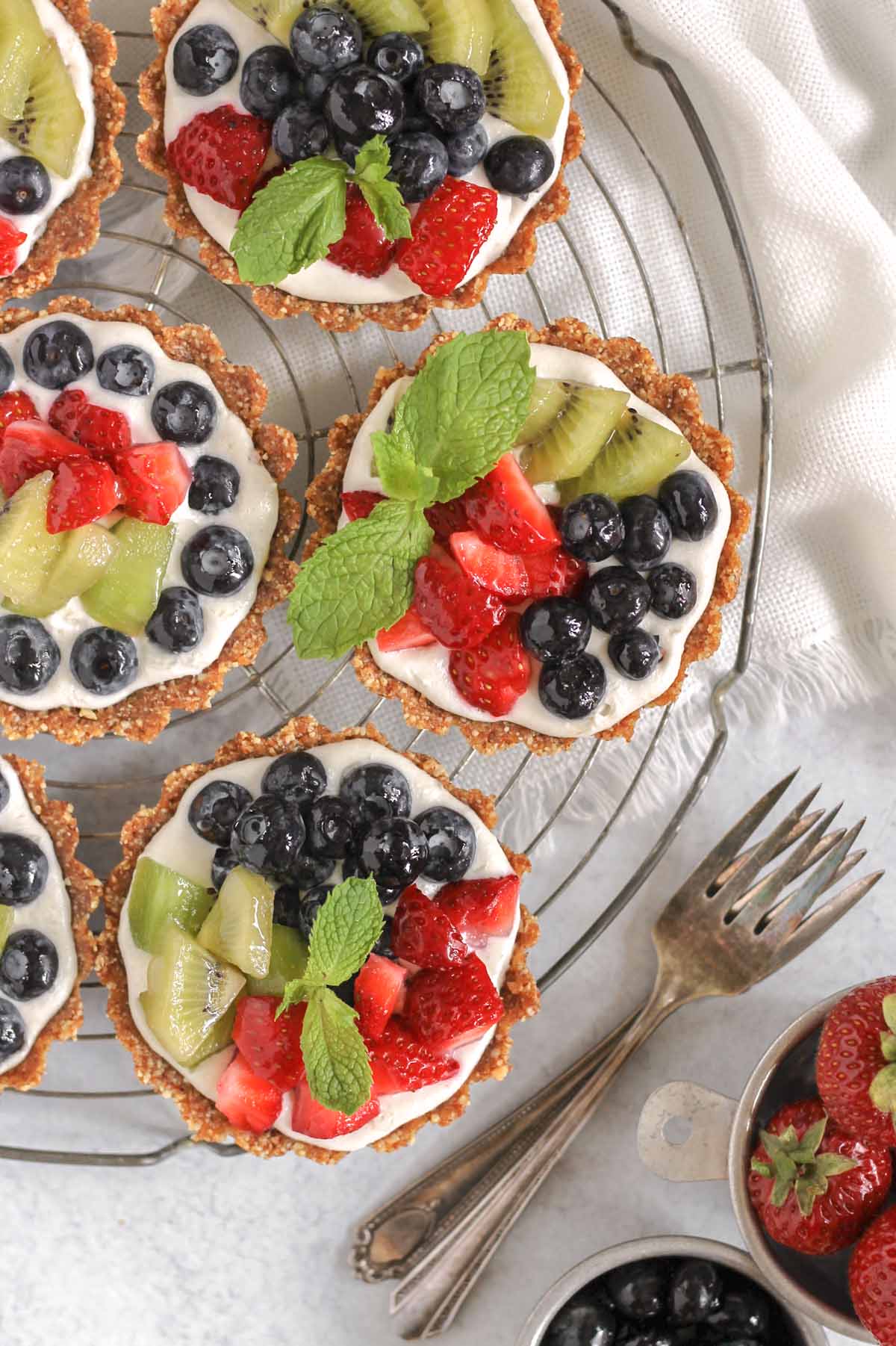 Mini vegan fruit tarts on a round wire cooling rack with two vintage forks off to the side.