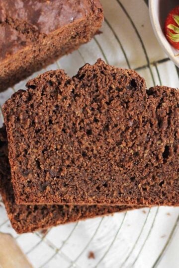 Two slices stacked of chocolate protein banana bread on a round wire cooling rack with a bowl of strawberries to the side.