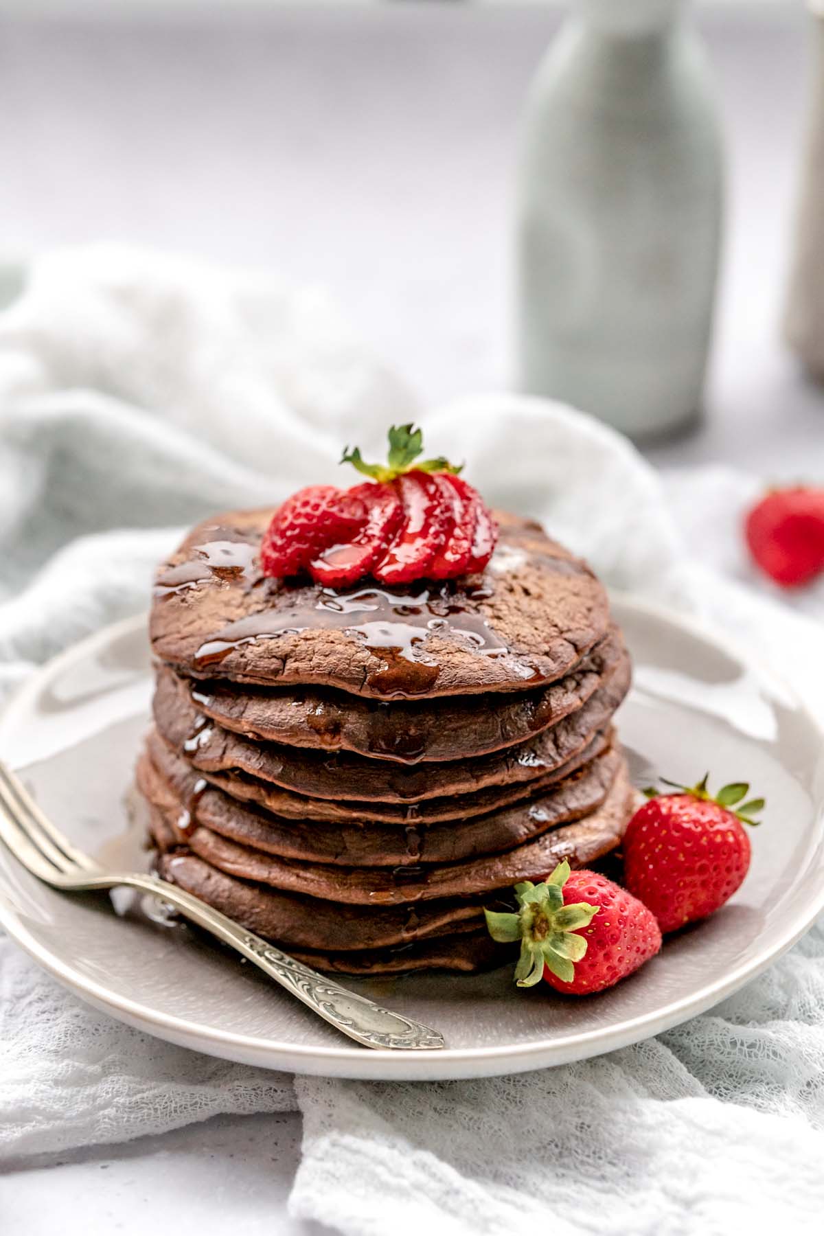 Chocolate pancakes topped with strawberries and dripping with syrup on a plate with a vintage fork.