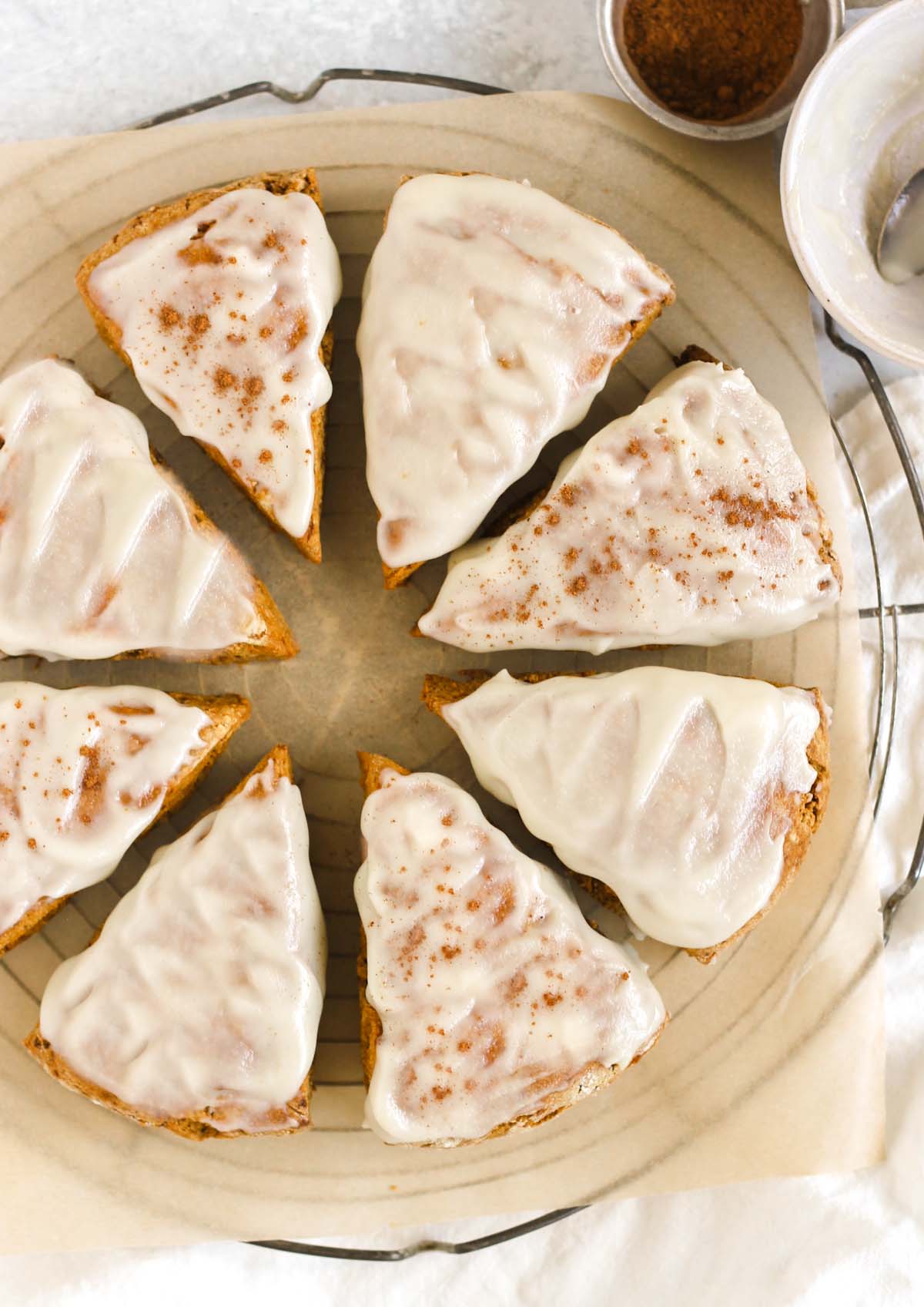 Eight frosted pumpkin scones on a round cooling rack.