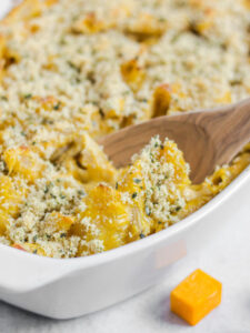 Baked mac and cheese topped with a sage/bread crumb mix in a white baking dish with a wooden spoon.
