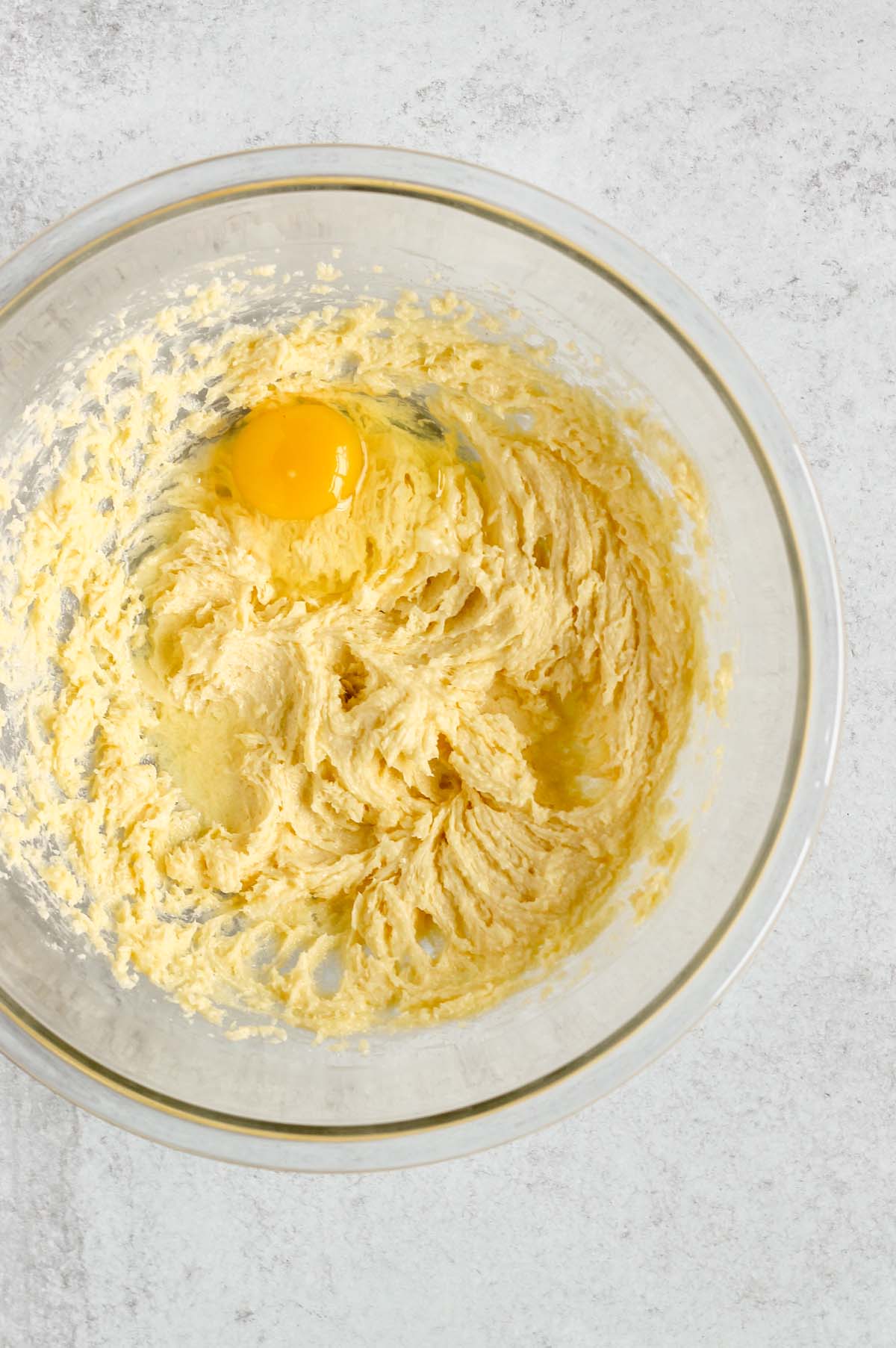 Butter and sugar creamed with an egg added in a glass mixing bowl.